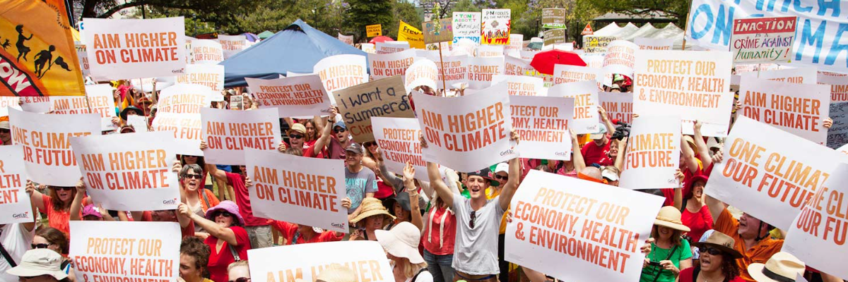 GetUp members protesting with signs saying "aim higher on climate"
