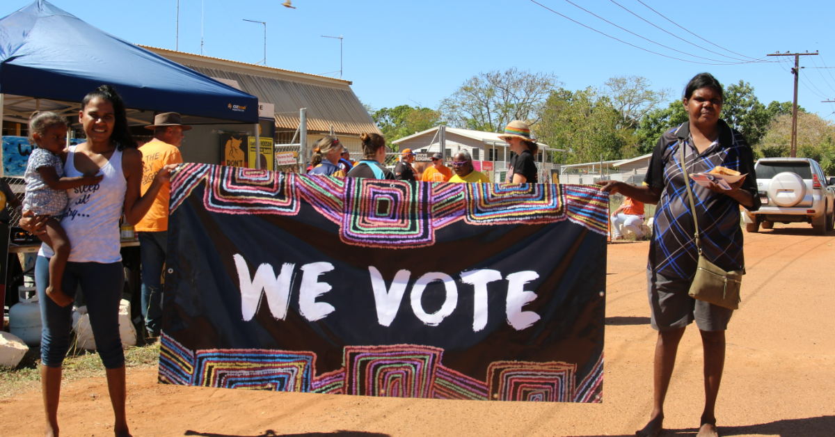 People at a polling booth holding a sign saying "we vote"